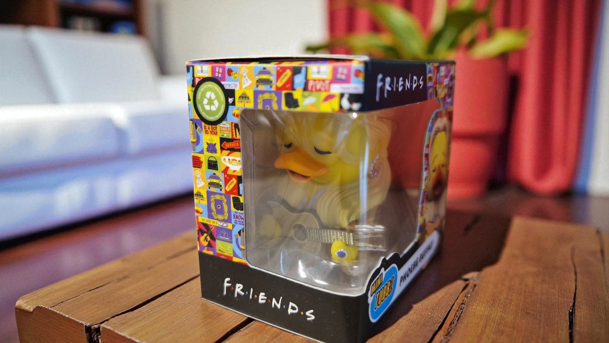 Rubber duck in a 'Friends' themed packaging on a wooden surface with a blurred background