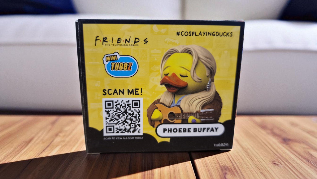 Product packaging for a duck toy inspired by 'Friends' with a QR code on a wooden surface.