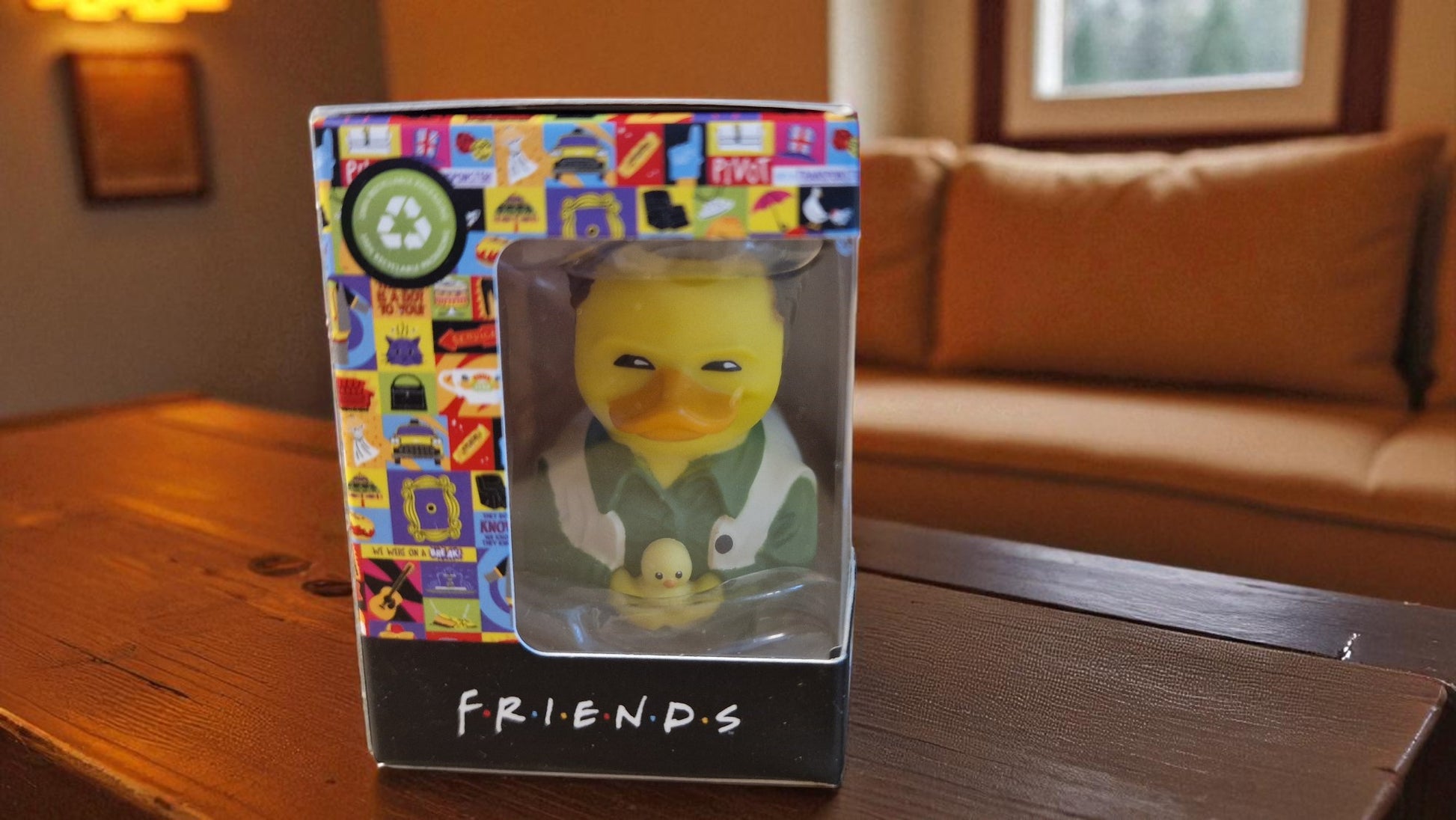 Rubber duck toy in a 'Friends' themed box on a wooden table.