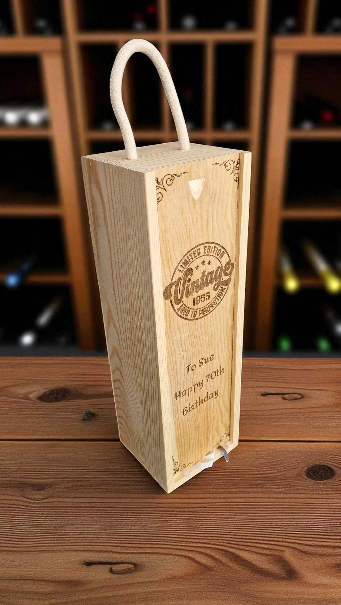 Wooden wine box with engraved text on a wooden surface, blurred wine bottles in the background