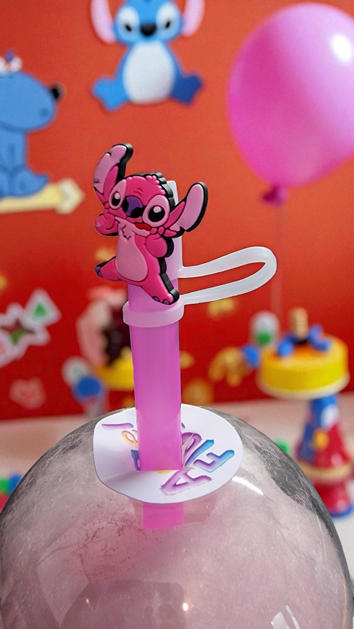 Pink character straw with a colorful background featuring cartoon characters and balloons.