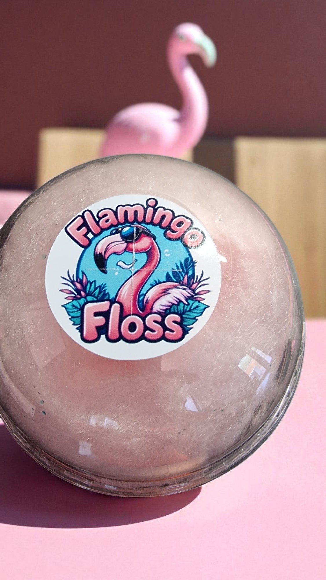 Ball with 'Flamingo Floss' sticker on a pink surface with a blurred flamingo in the background