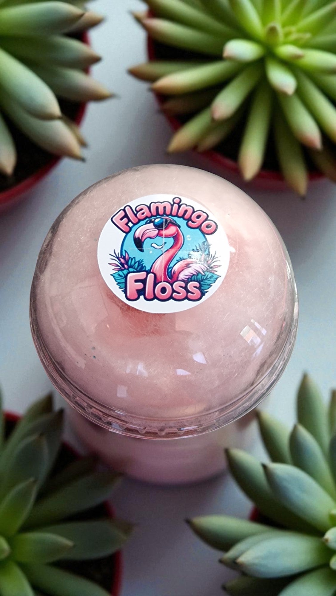 Pink floss container with a flamingo-themed sticker surrounded by succulents