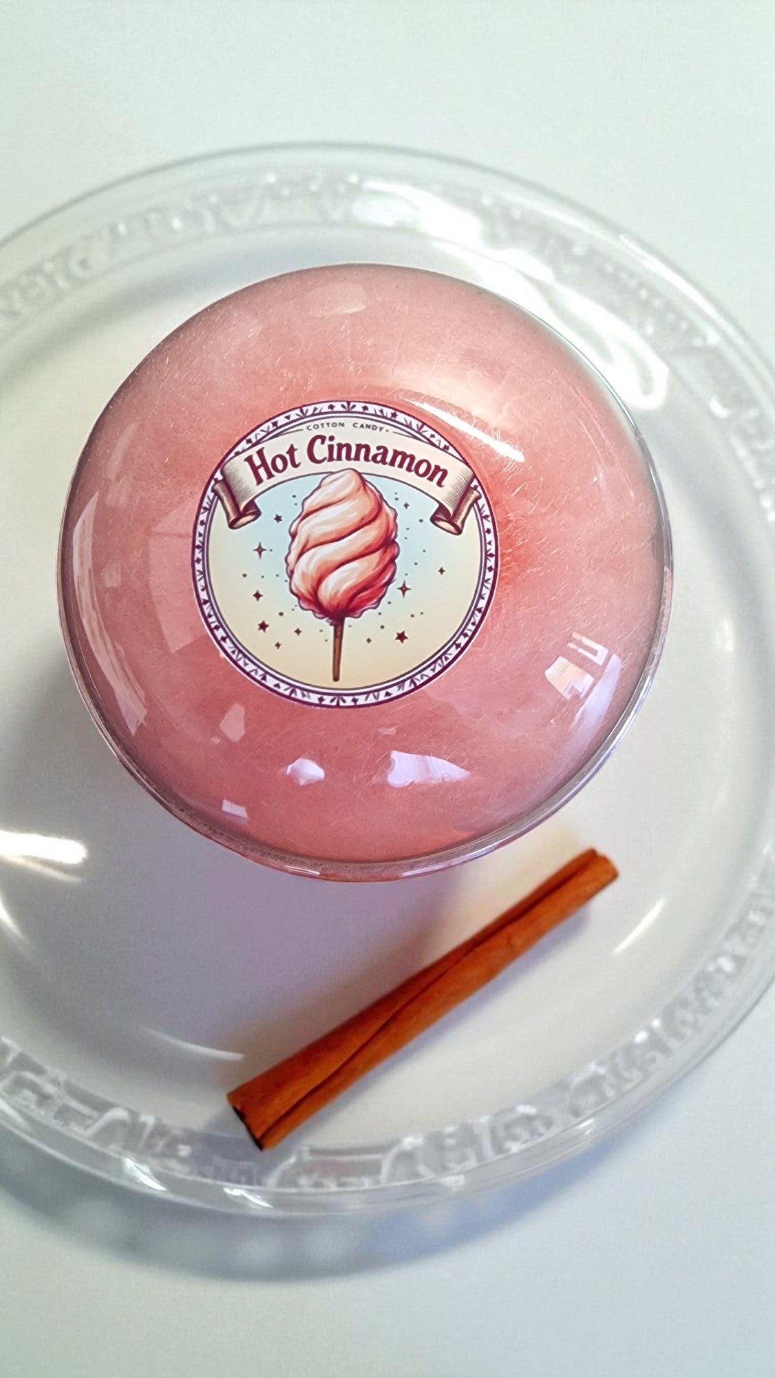 Pink hot cinnamon roll in a clear container with a cinnamon stick on a white background