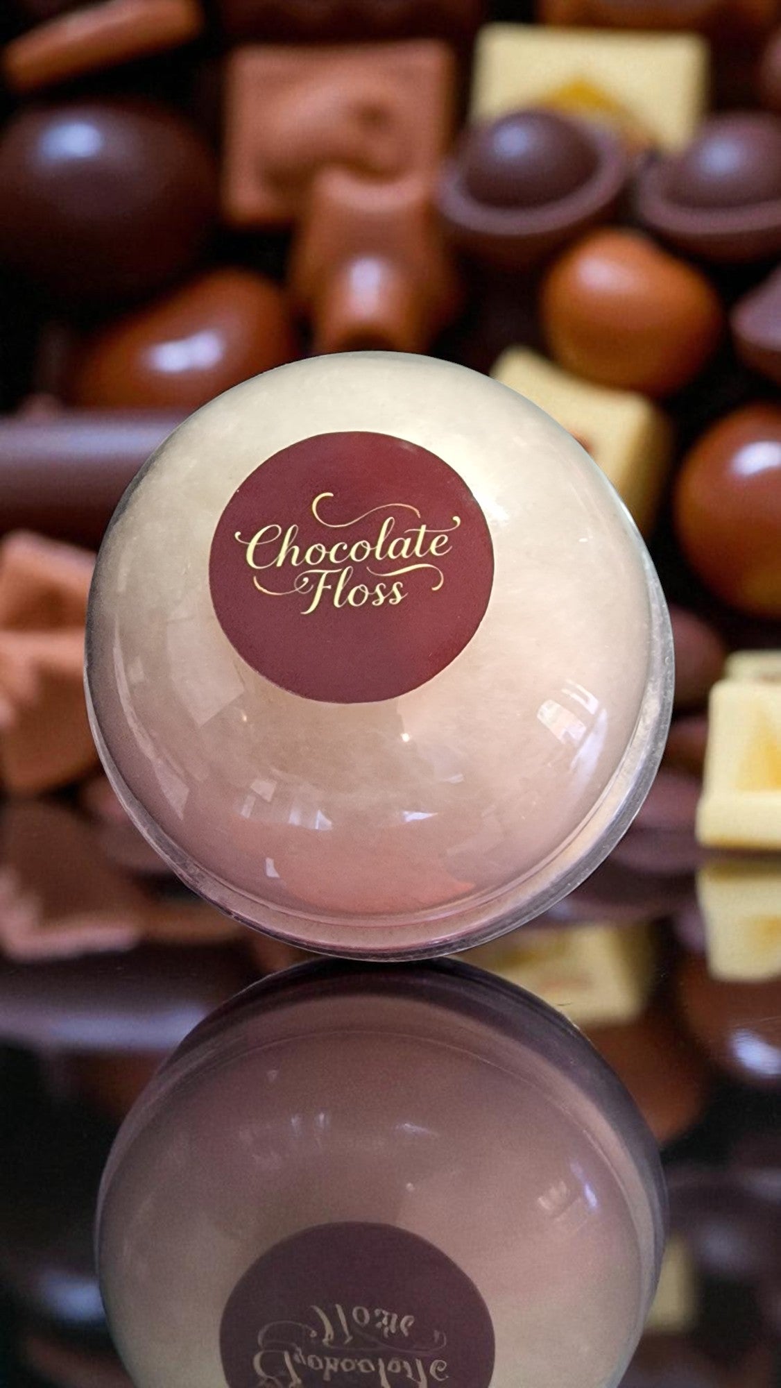 Chocolate floss ball with a visible brand label against a background of assorted chocolates.