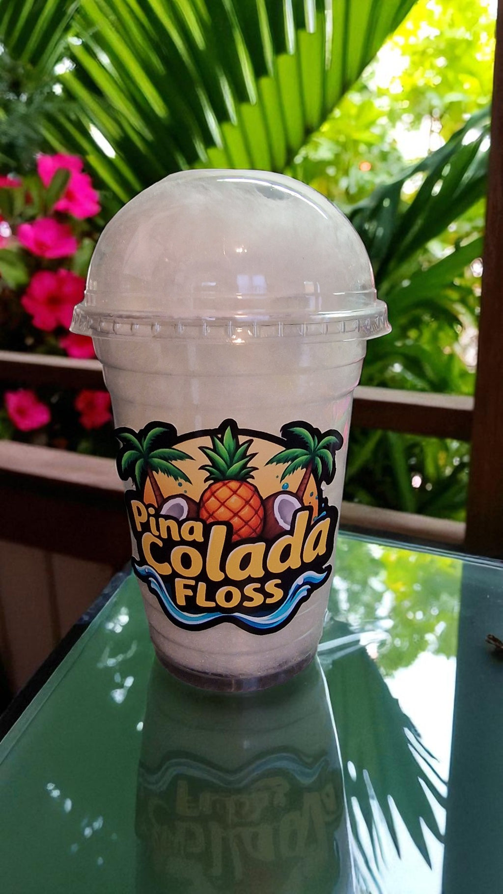 Pina Colada Floss drink in a clear plastic cup with a tropical design on a reflective surface.