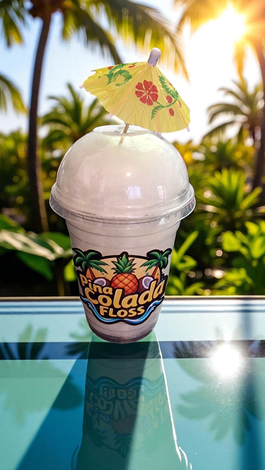 Pina Colada Floss drink with a decorative umbrella on a reflective surface with palm trees in the background.