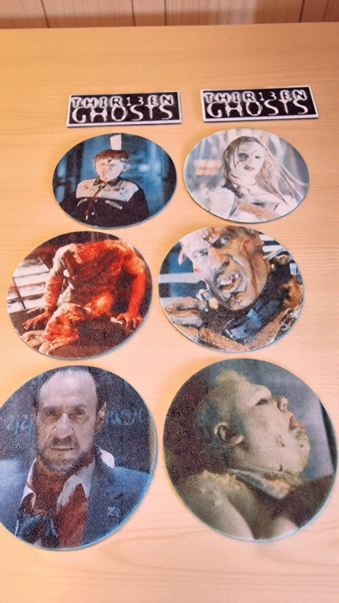 Set of circular coasters with images of people and animals on a wooden surface, featuring 'The Ghosts' branding.