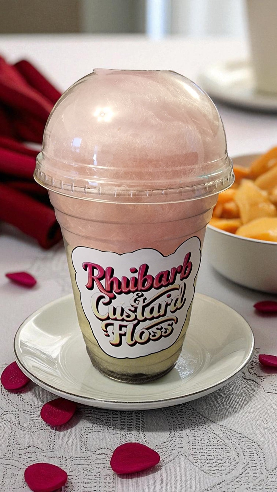Pink milkshake in a transparent cup with a label on a white plate, surrounded by rose petals.