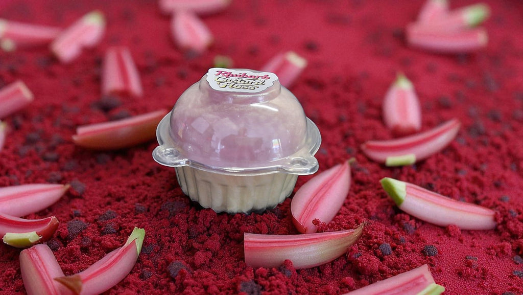 Small pink dessert in a clear dome on a red surface with rhubarb leaves.