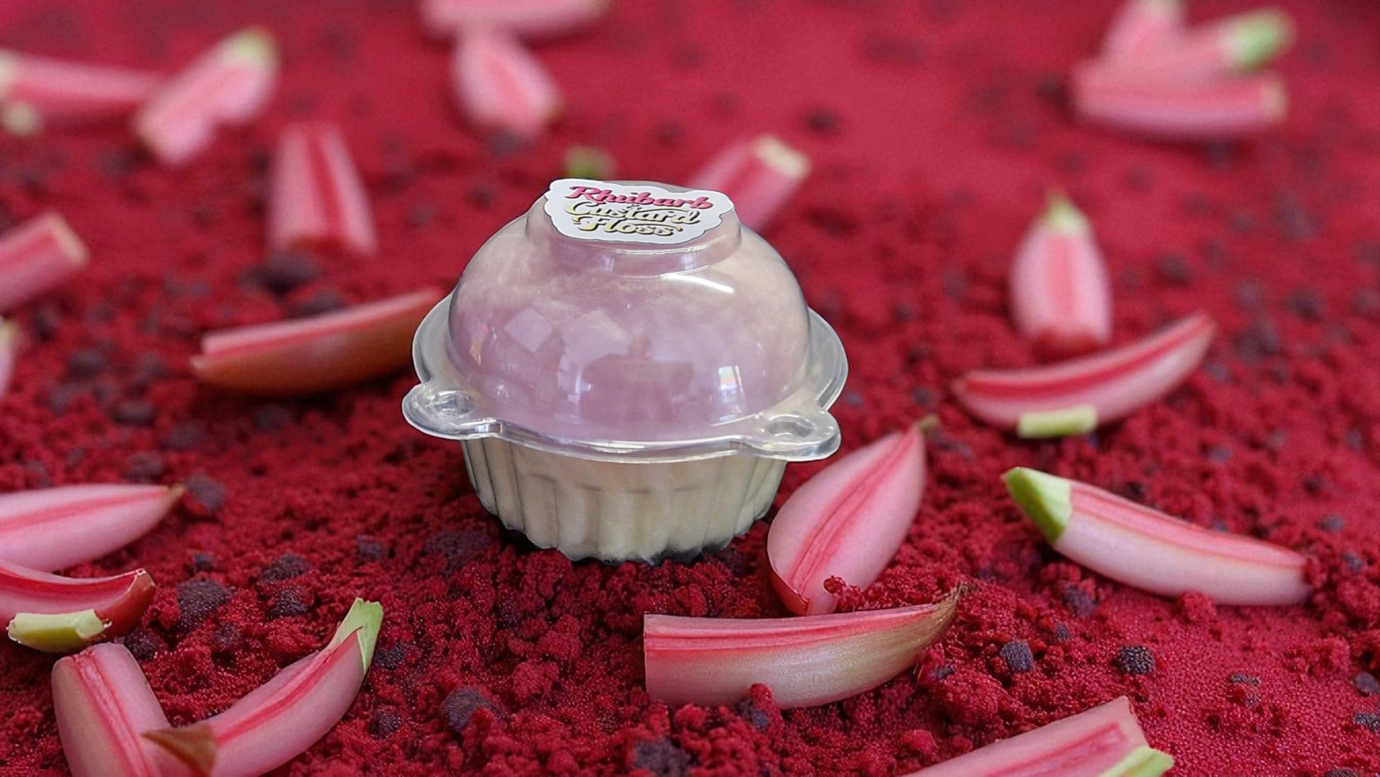 Small pink dessert in a clear dome on a red surface with rhubarb leaves.