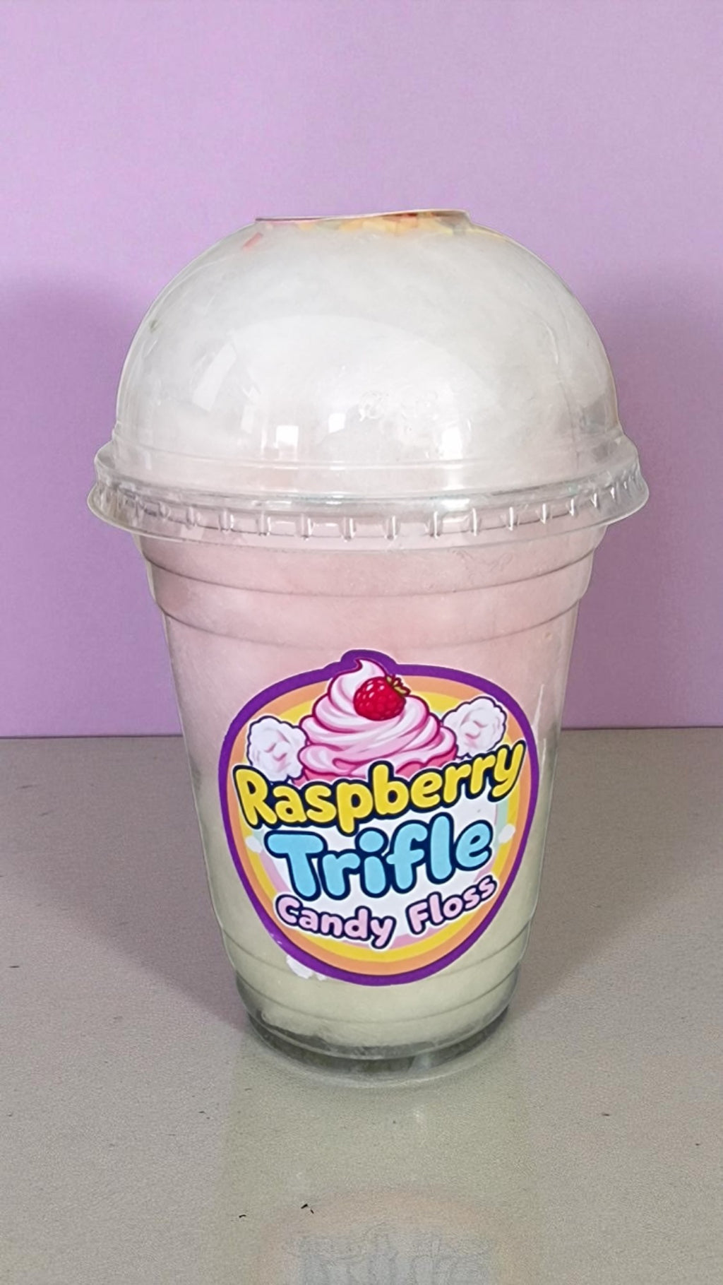 Raspberry Trifle candy floss in a clear cup with a purple lid against a light purple background