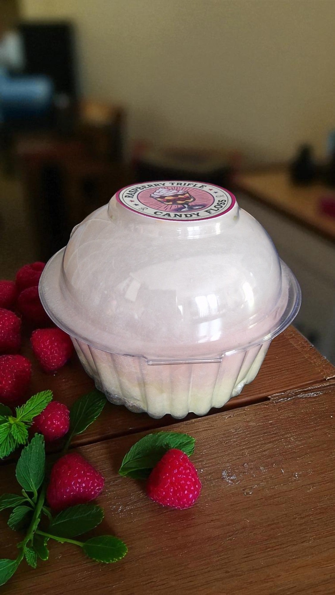 Pink cupcake-shaped container with a lid on a wooden surface with raspberries and mint leaves.