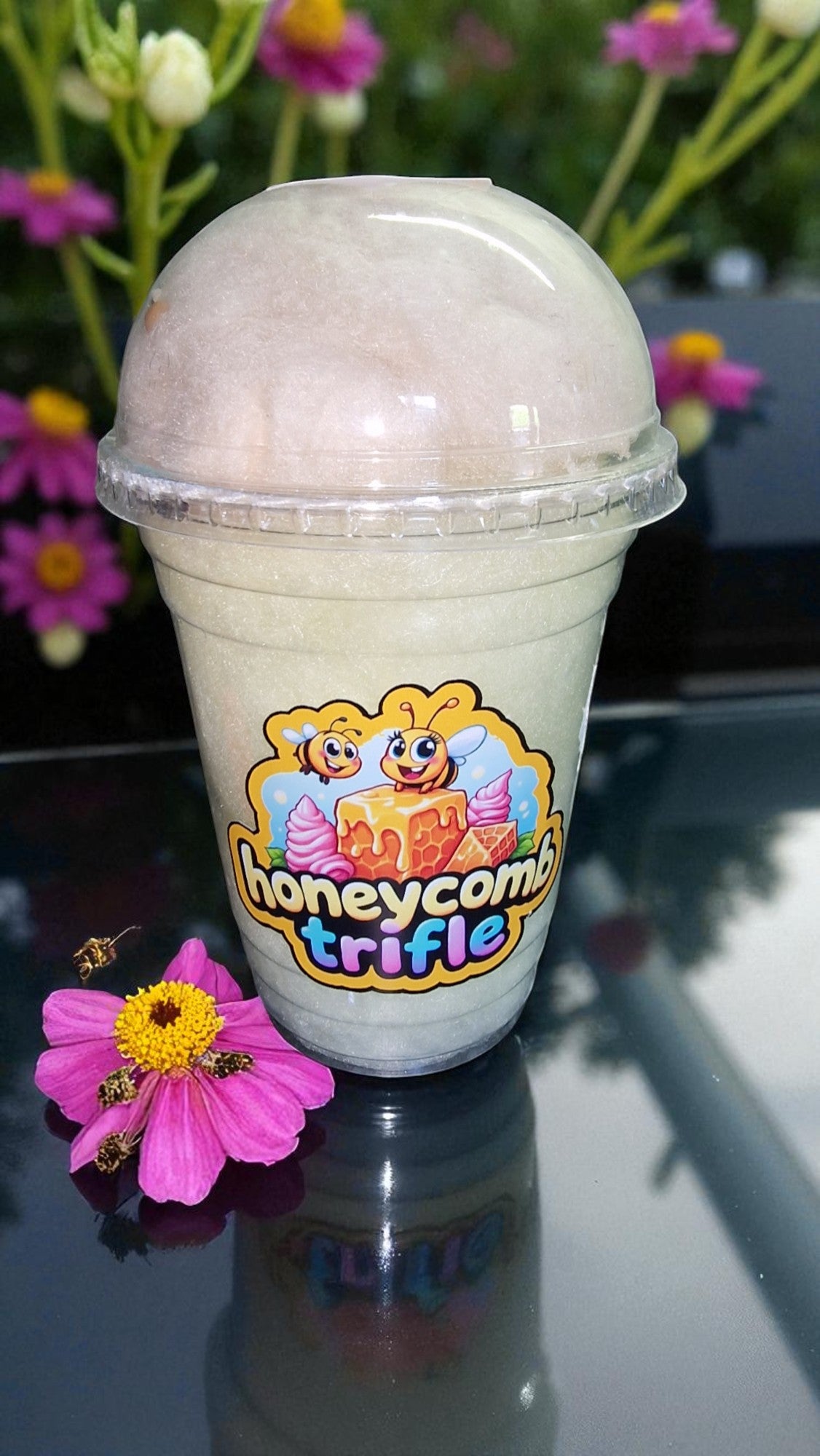 Ice cream cup with 'Honeycomb Trifle' logo on a reflective surface with flowers in the background