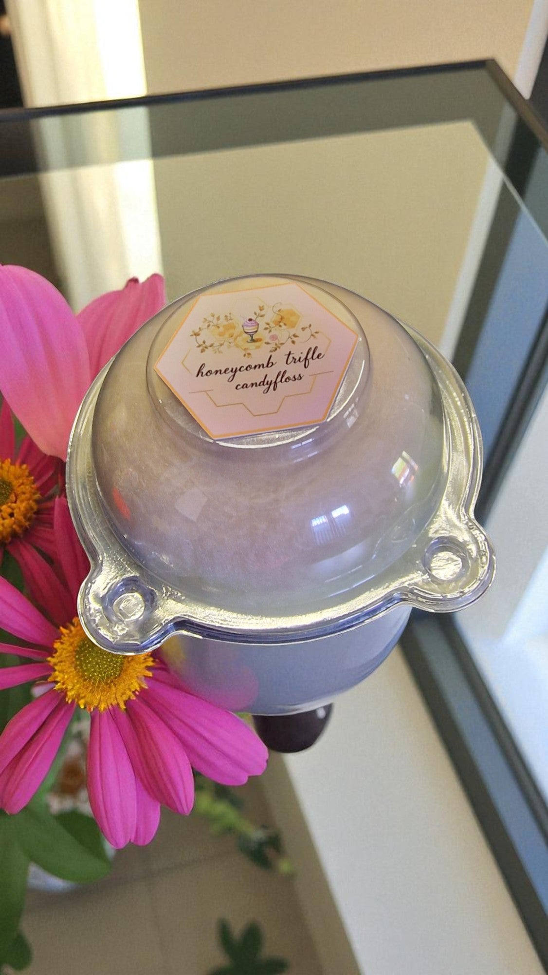 Candle with a decorative label next to a pink flower