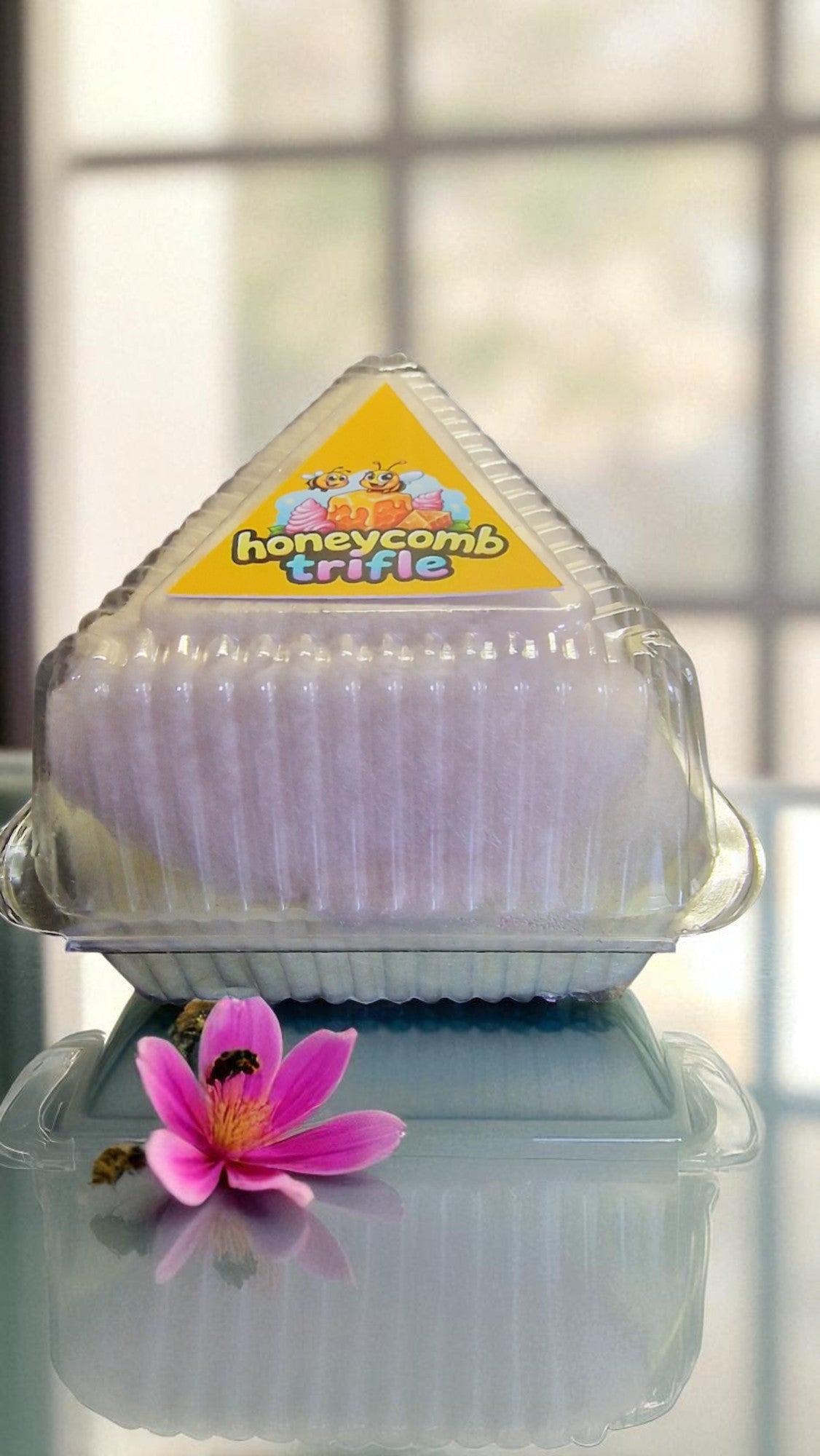 Packaged honeycomb trifle with a pink flower on a reflective surface