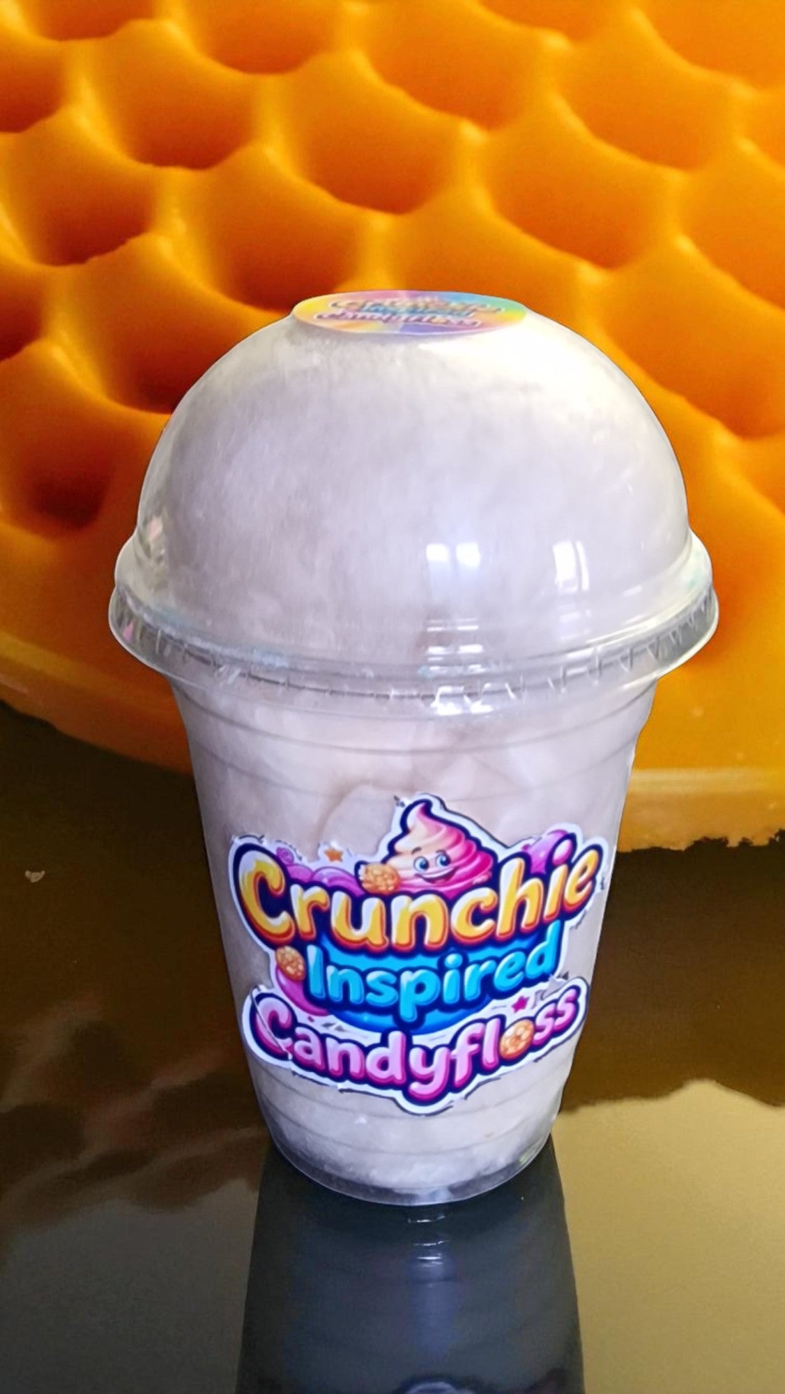 Clear cup with white fluffy treat labeled 'Crunchie Inspired Candyfloss' against a textured orange background