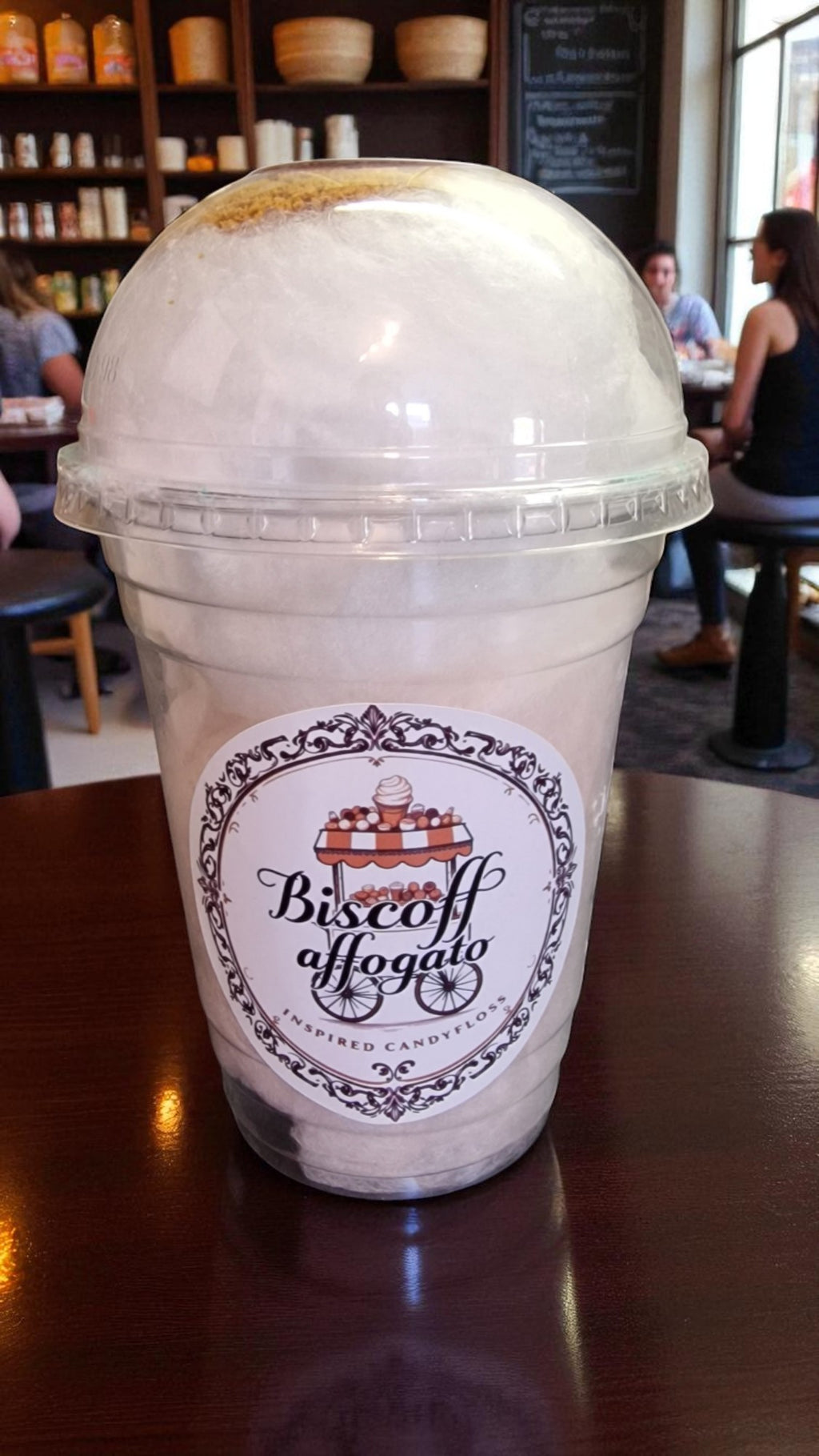 Biscoff Affogato drink in a clear plastic cup with a label on a wooden table in a cafe.