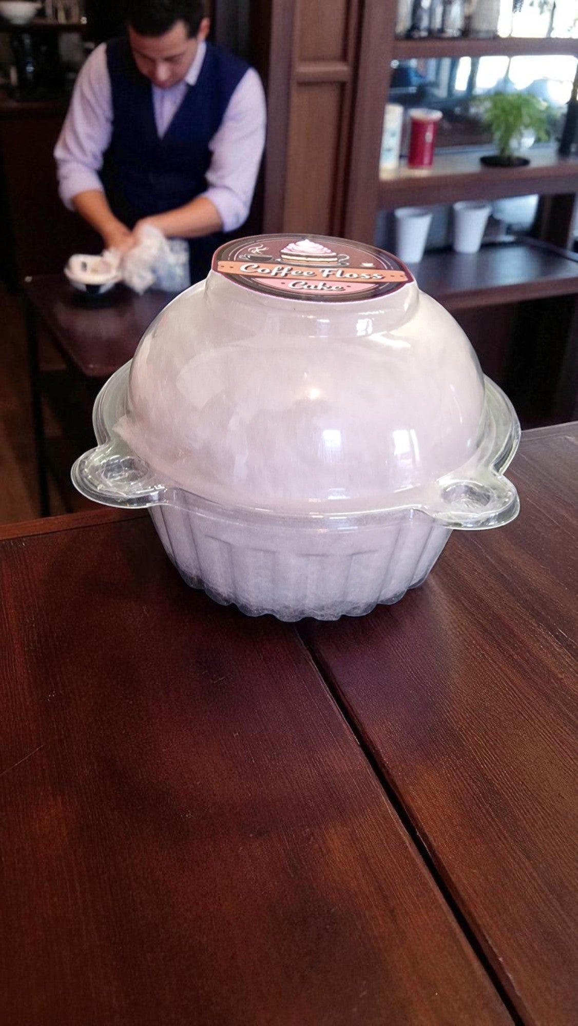 White ceramic dish with a lid on a wooden table, with a person in the background.