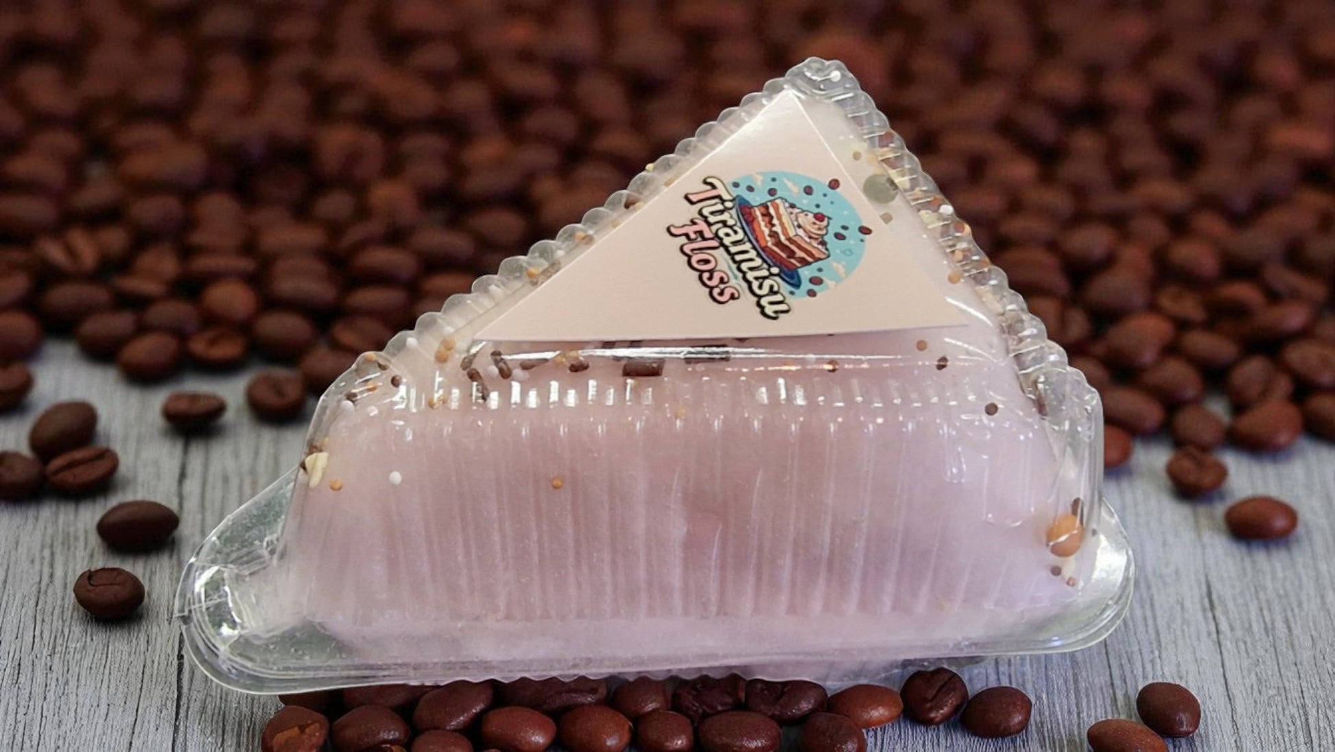 Triangular dessert in a clear plastic packaging with coffee beans on a wooden surface