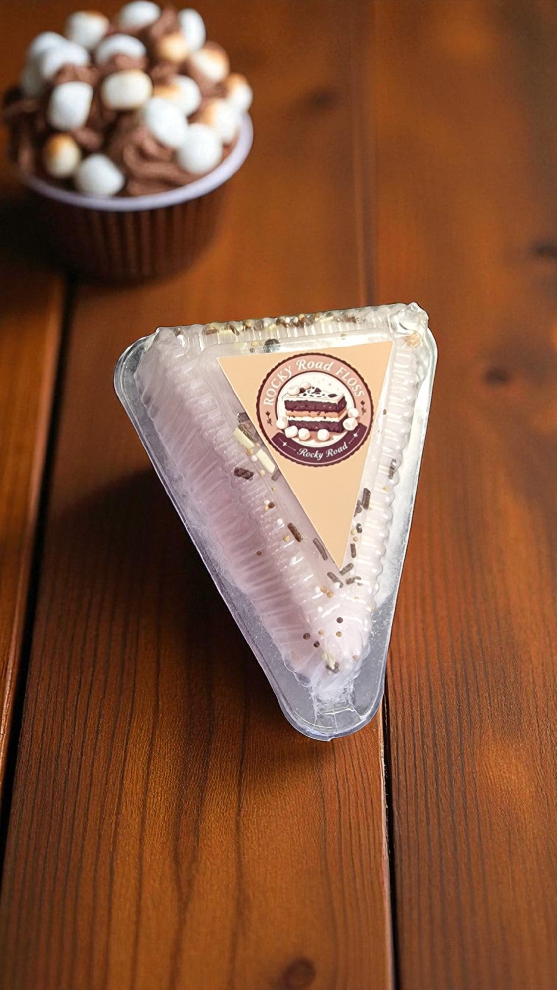 Triangular dessert in a clear plastic container on a wooden surface with a blurred background