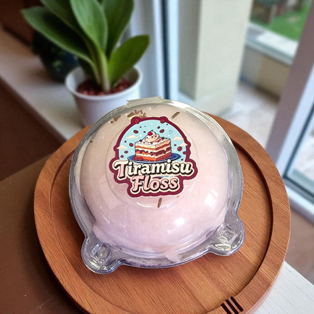 Tiramisu floss dessert in a clear container on a wooden board with a plant in the background.