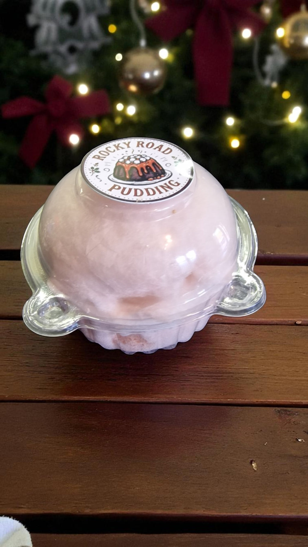 Pink pudding in a clear container with a Rocky Road Puddings label, set against a festive background.