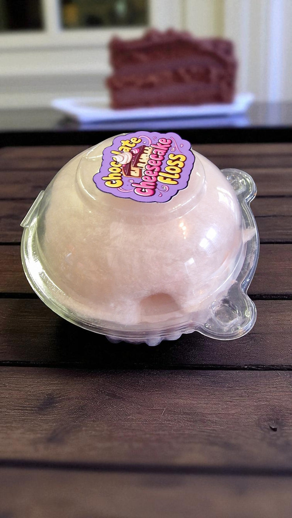 Bowl of pink ice cream with a 'Chocolate Strawberry Cheesecake Floss' label on a wooden surface.