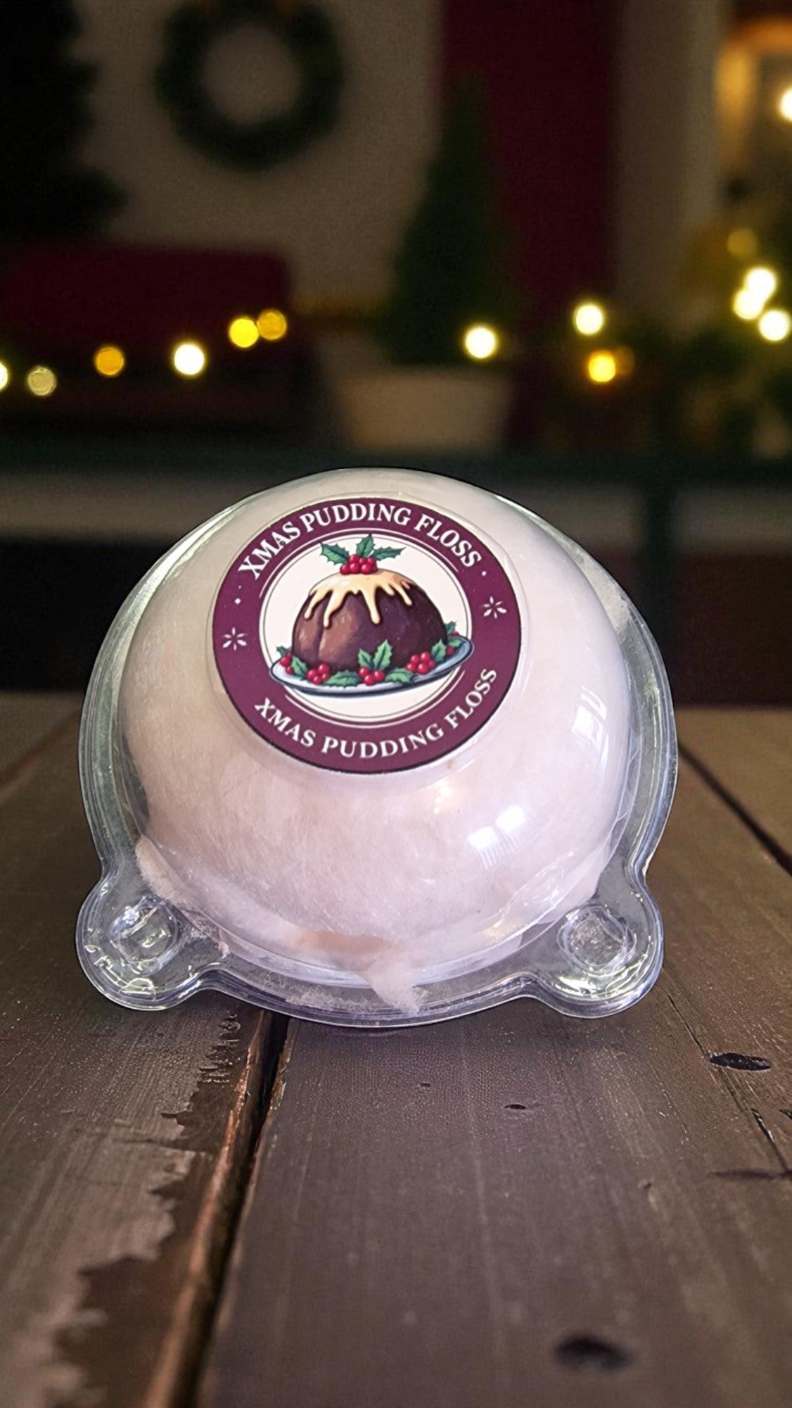 Xmas pudding floss ball with a label on a wooden surface, Christmas decorations in the background.
