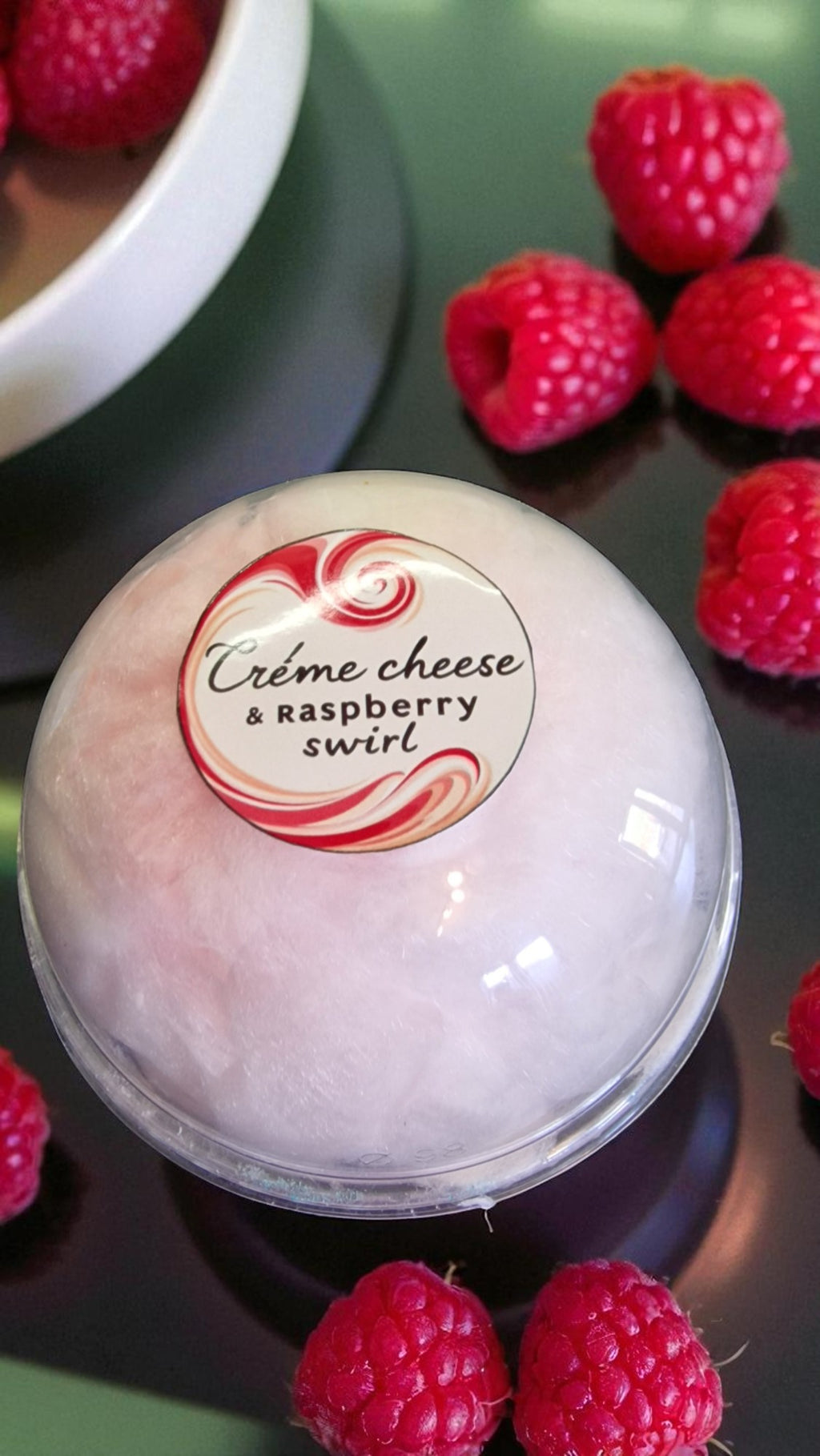 Bowl of creme cheese and raspberry swirl dessert with raspberries around it.