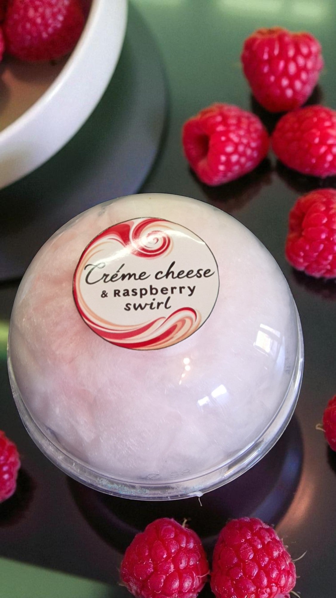 Bowl of creme cheese and raspberry swirl dessert with raspberries around it.