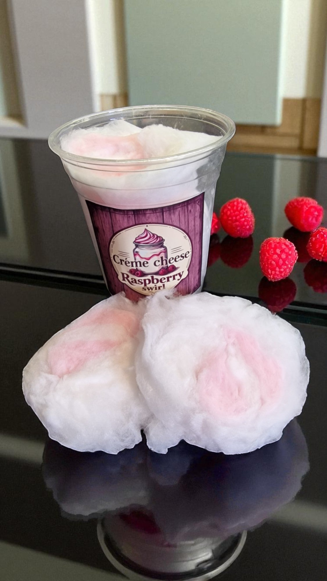 Cup of raspberry ice cream with two pink cotton candy balls on a reflective surface.