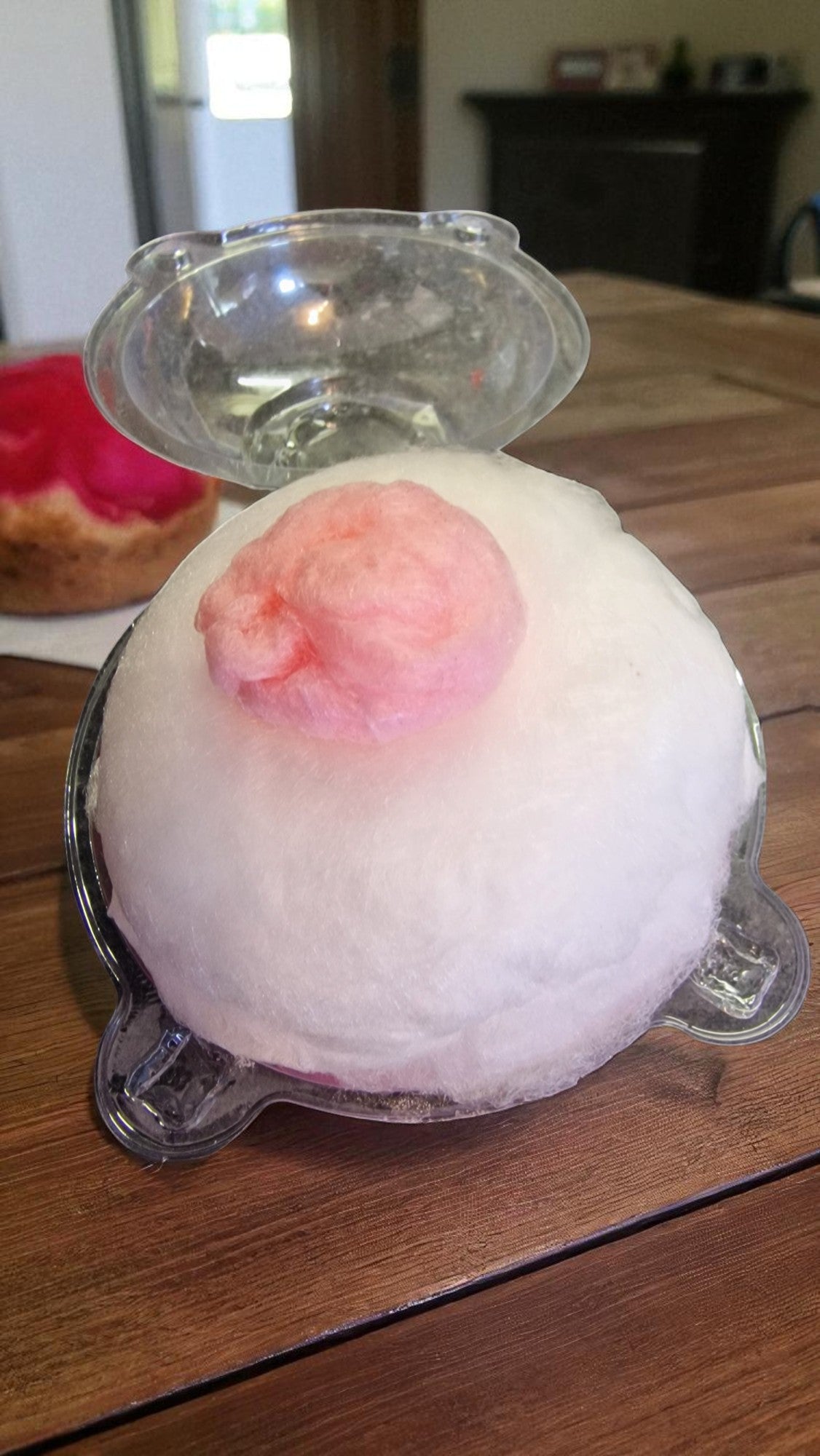 Pink and white bath bomb in a clear plastic container on a wooden surface.