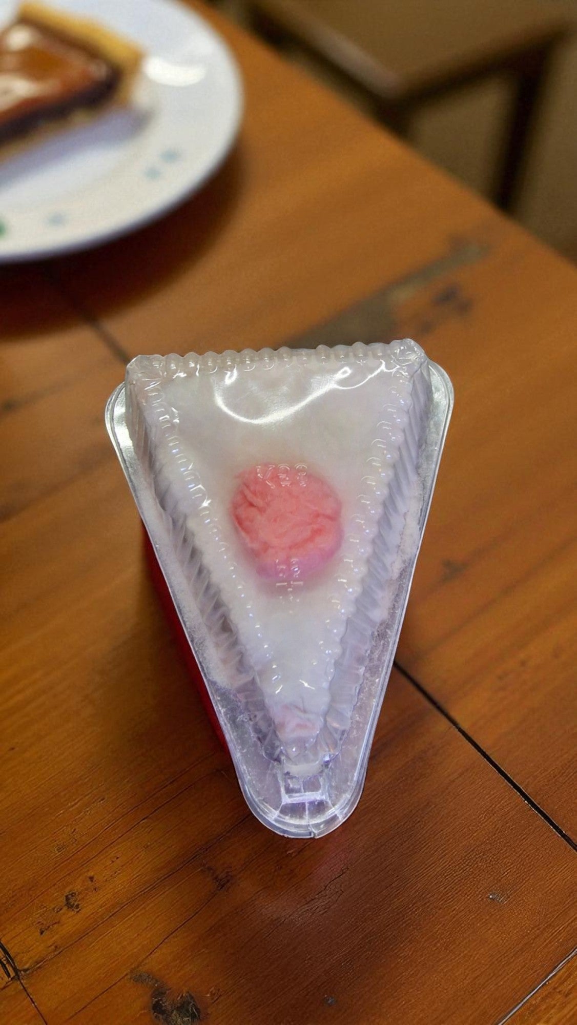 Small triangular dessert with pink topping on a wooden table