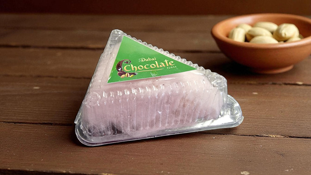 Packaged chocolate on a wooden surface with a bowl of nuts in the background