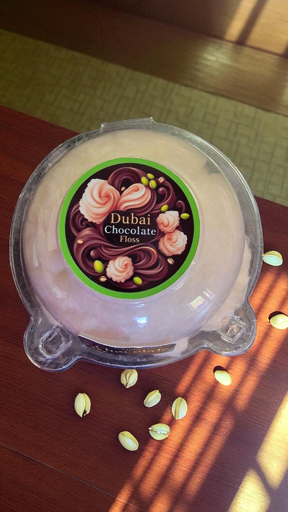 Container of Dubai Chocolate Floss on a wooden surface with scattered floss pieces.