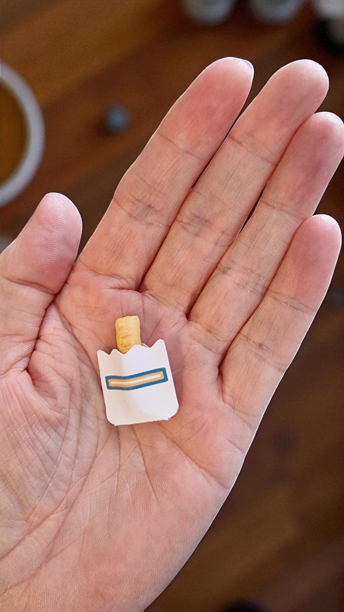 Small toy figure of a bear with a blue ribbon held in a hand on a wooden surface.