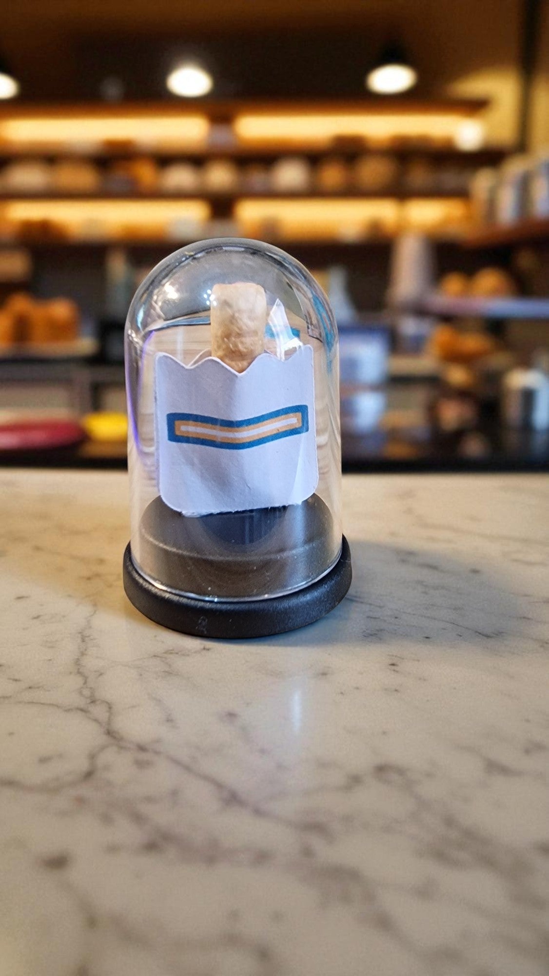 Small glass dome with a paper towel inside on a marble surface, blurred background of shelves.