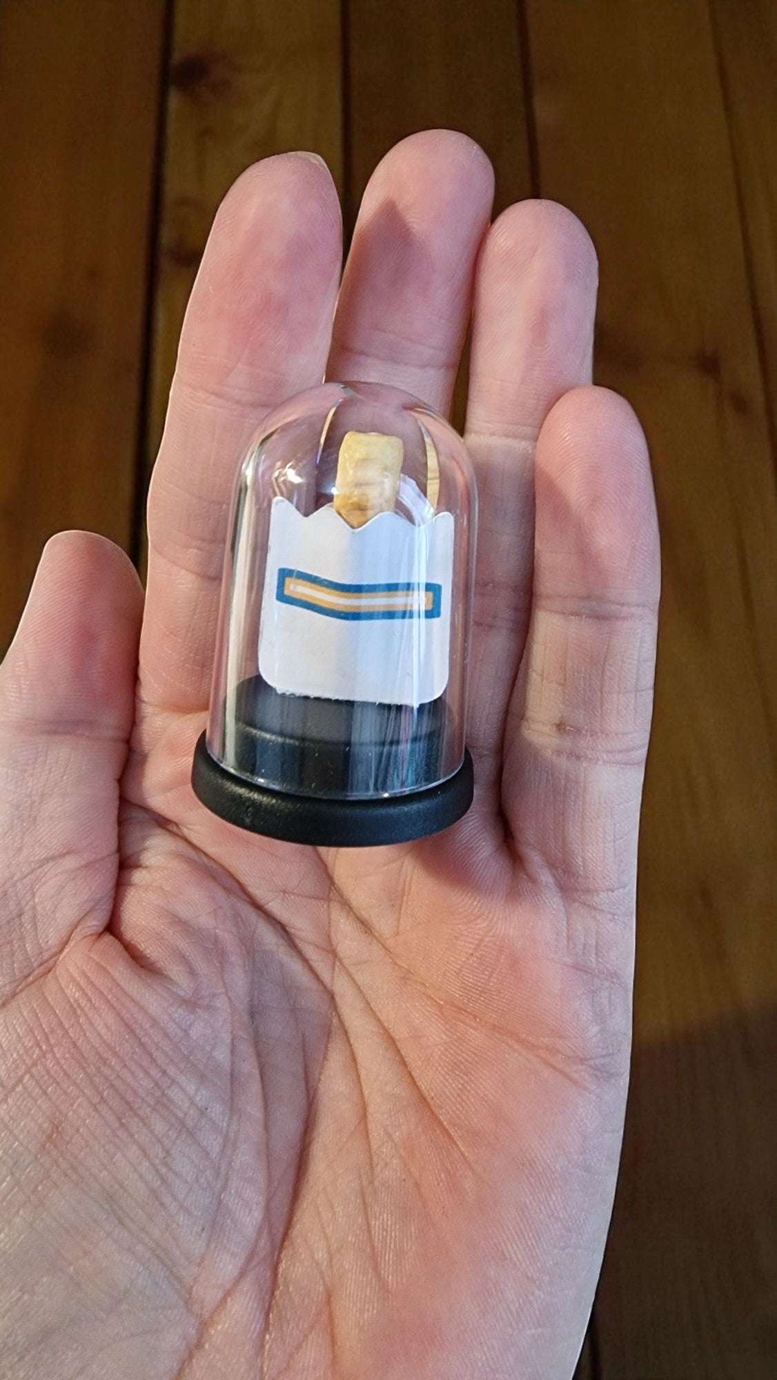 Small transparent container with a label held in a hand against a wooden background