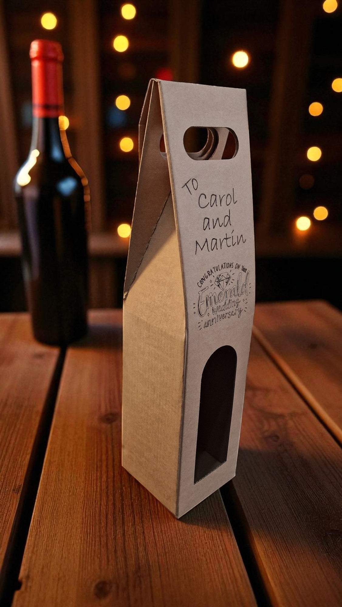 Cardboard wine bottle box with cutout for a bottle on a wooden surface with blurred lights in the background