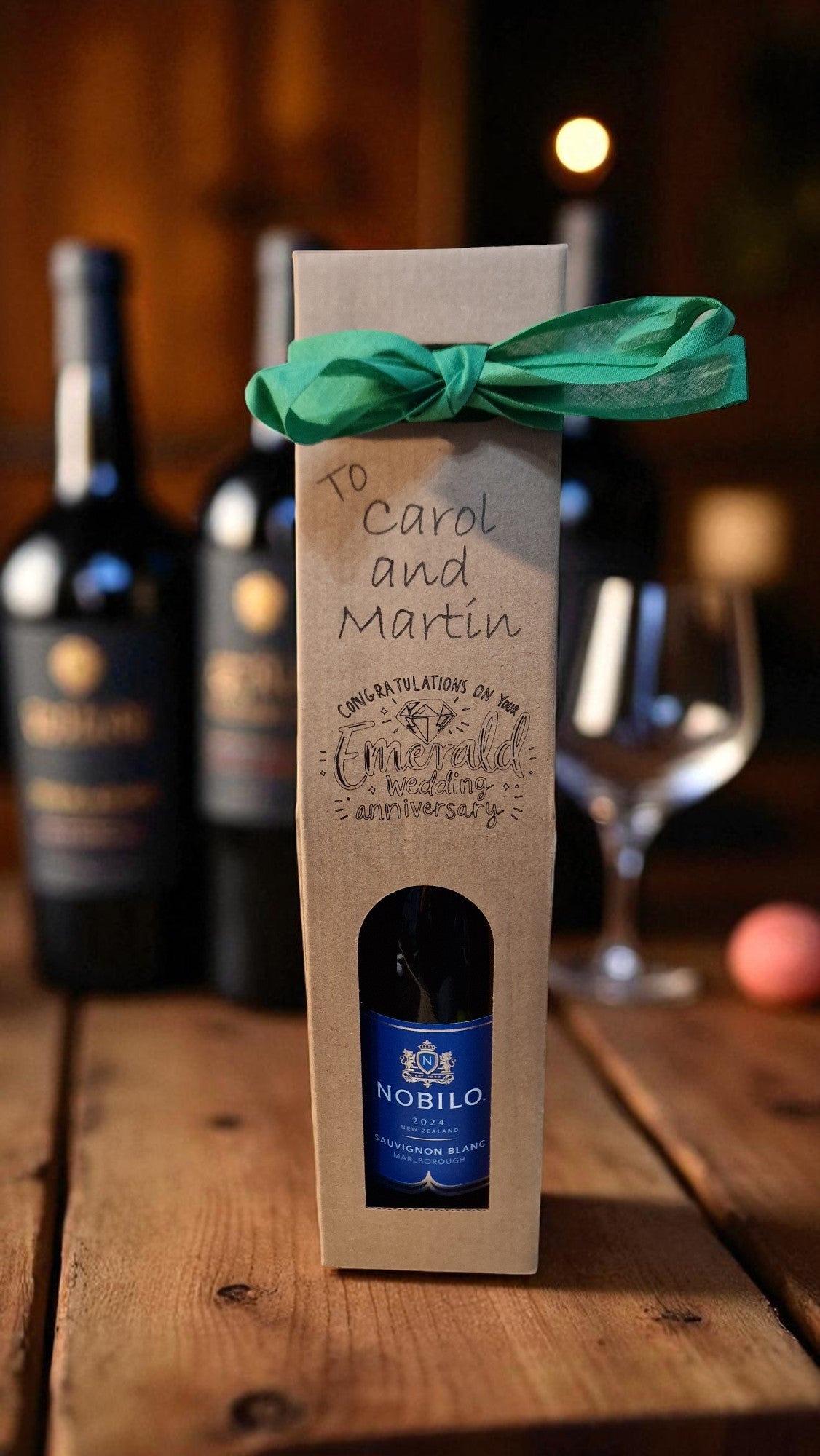 Gift box with a bottle of Nobilo wine on a wooden table with wine bottles and glasses in the background.