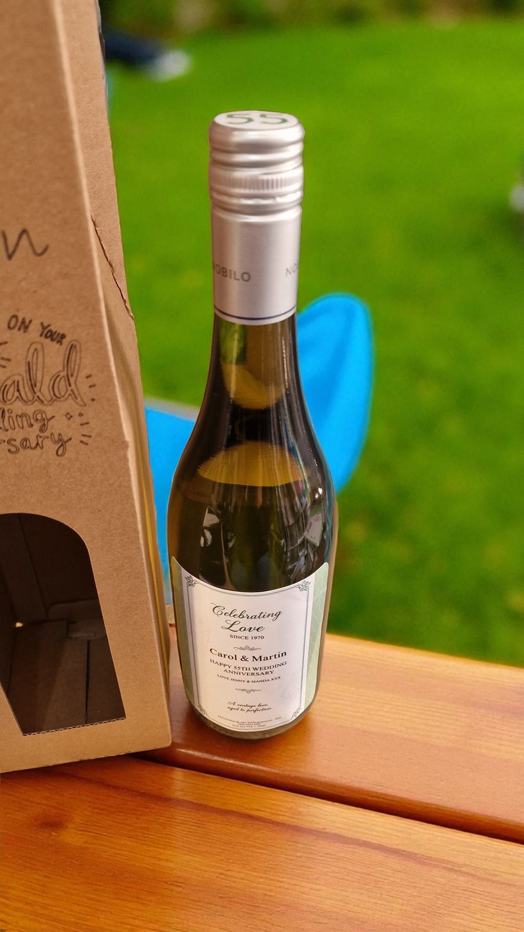Bottle of white wine on a wooden surface with a blurred green outdoor background
