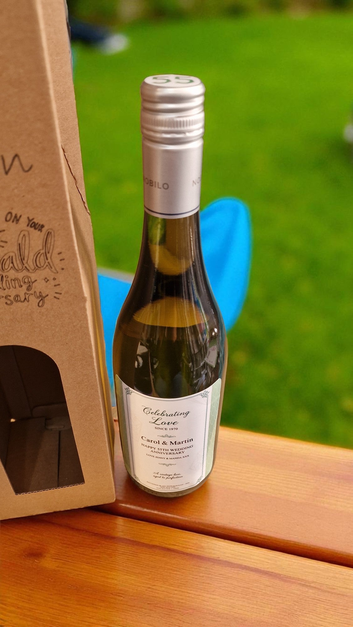 Bottle of white wine on a wooden surface with a blurred green outdoor background