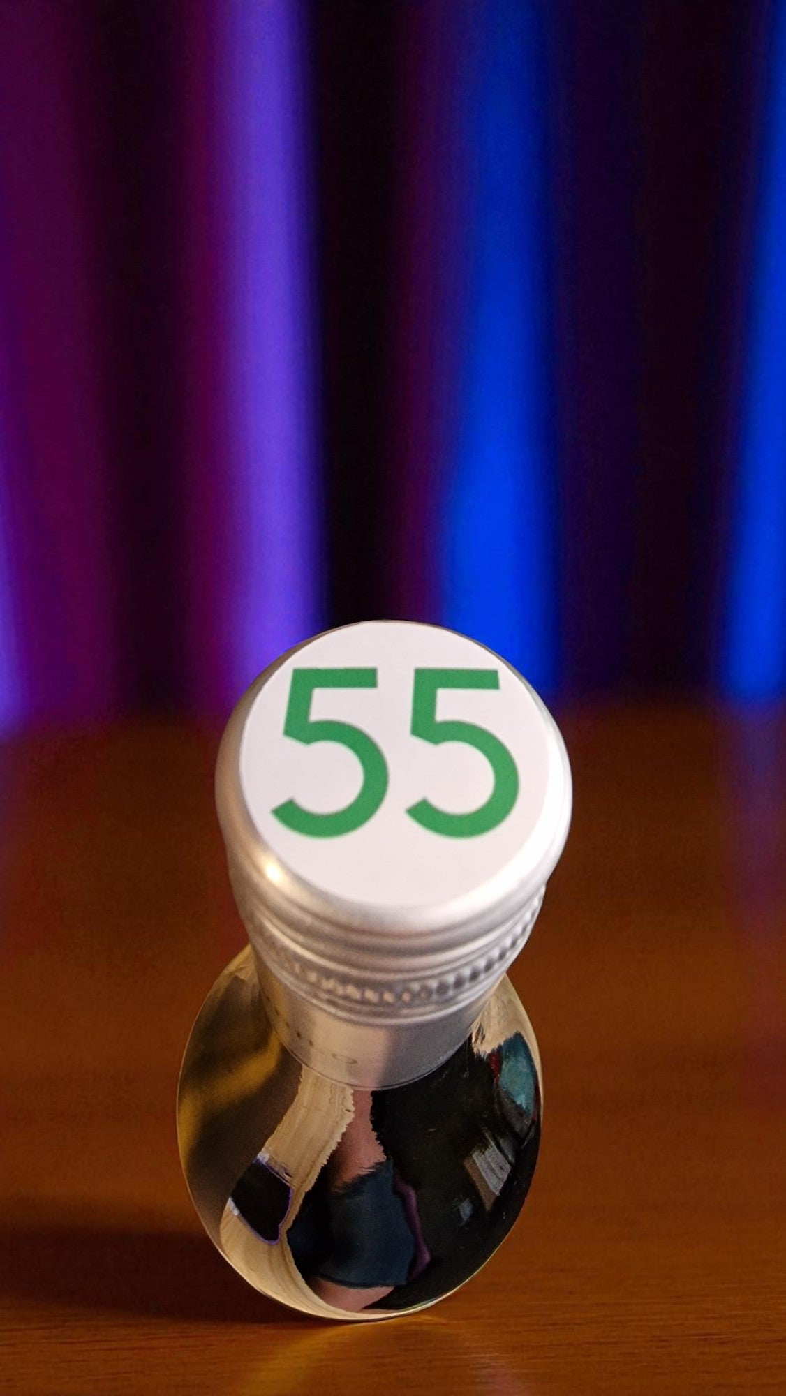 Bottle with a white cap labeled '55' on a wooden surface with a colorful curtain background.