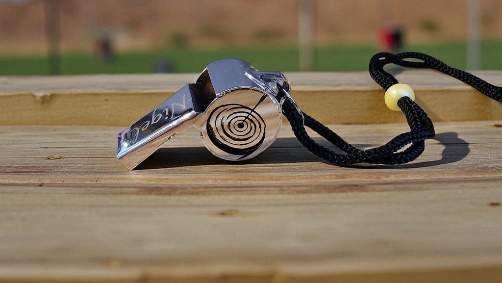 Metallic whistle with a black cord on a wooden surface