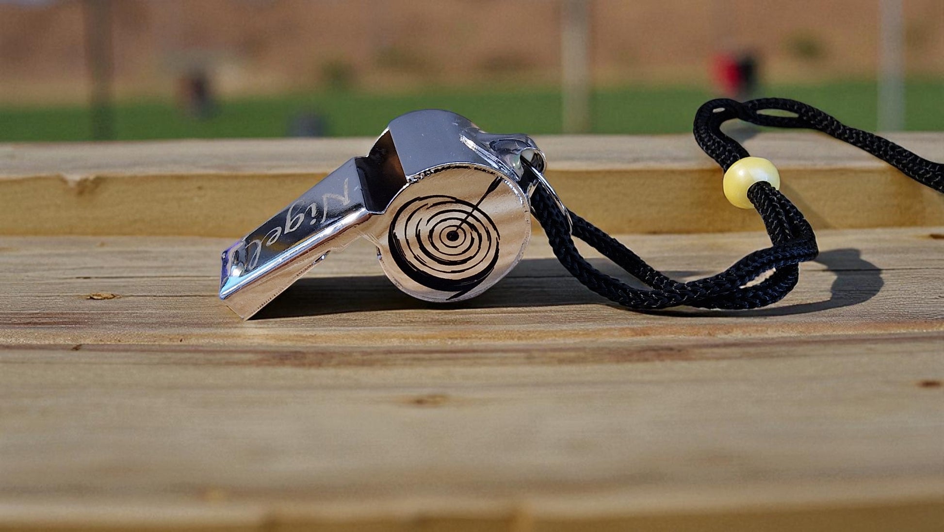 Metallic whistle with a black cord on a wooden surface