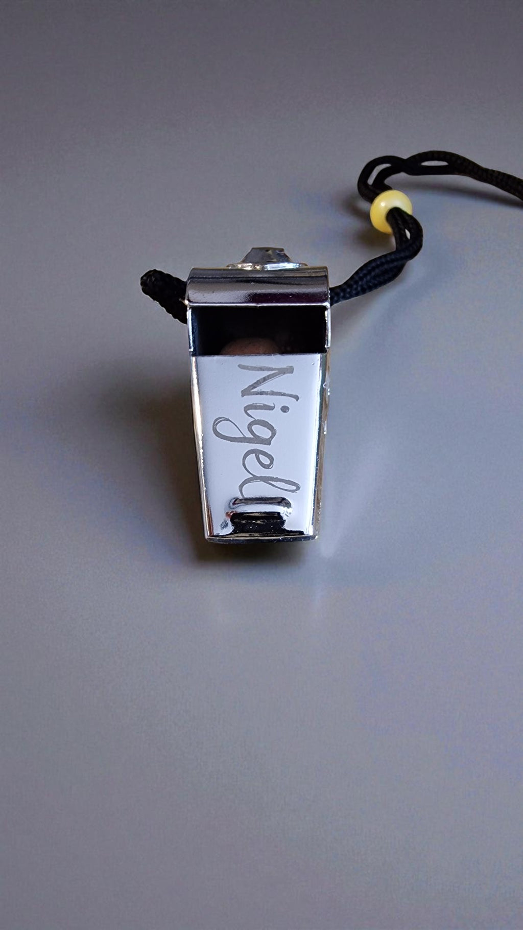 Metallic whistle with 'Nigel' engraved on a gray background