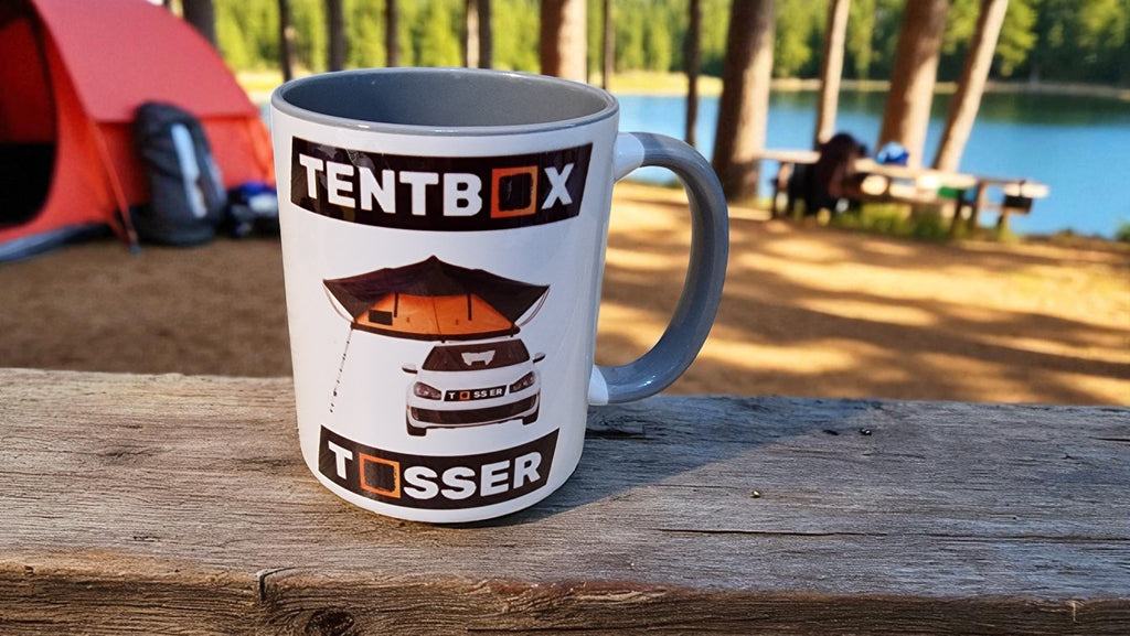 TentBox Tossler mug on a wooden surface with a camping scene in the background