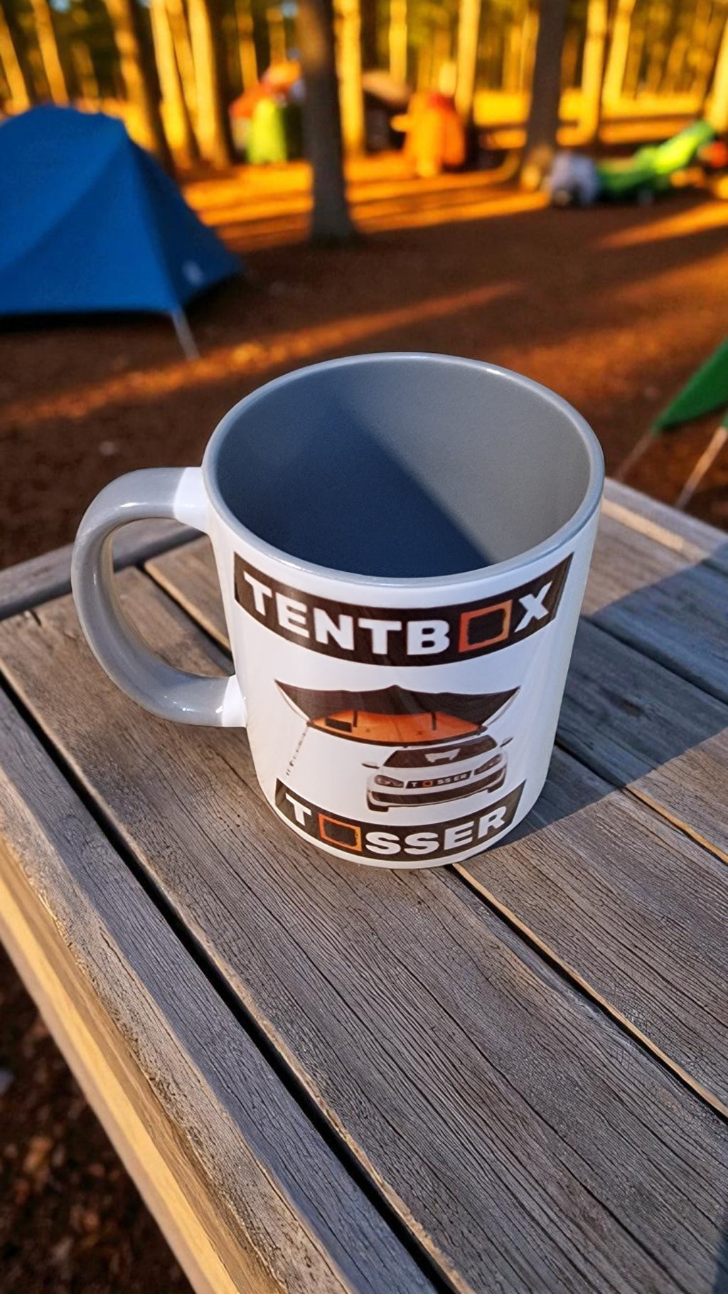 Mug with 'Tentbox' branding on a wooden surface outdoors.
