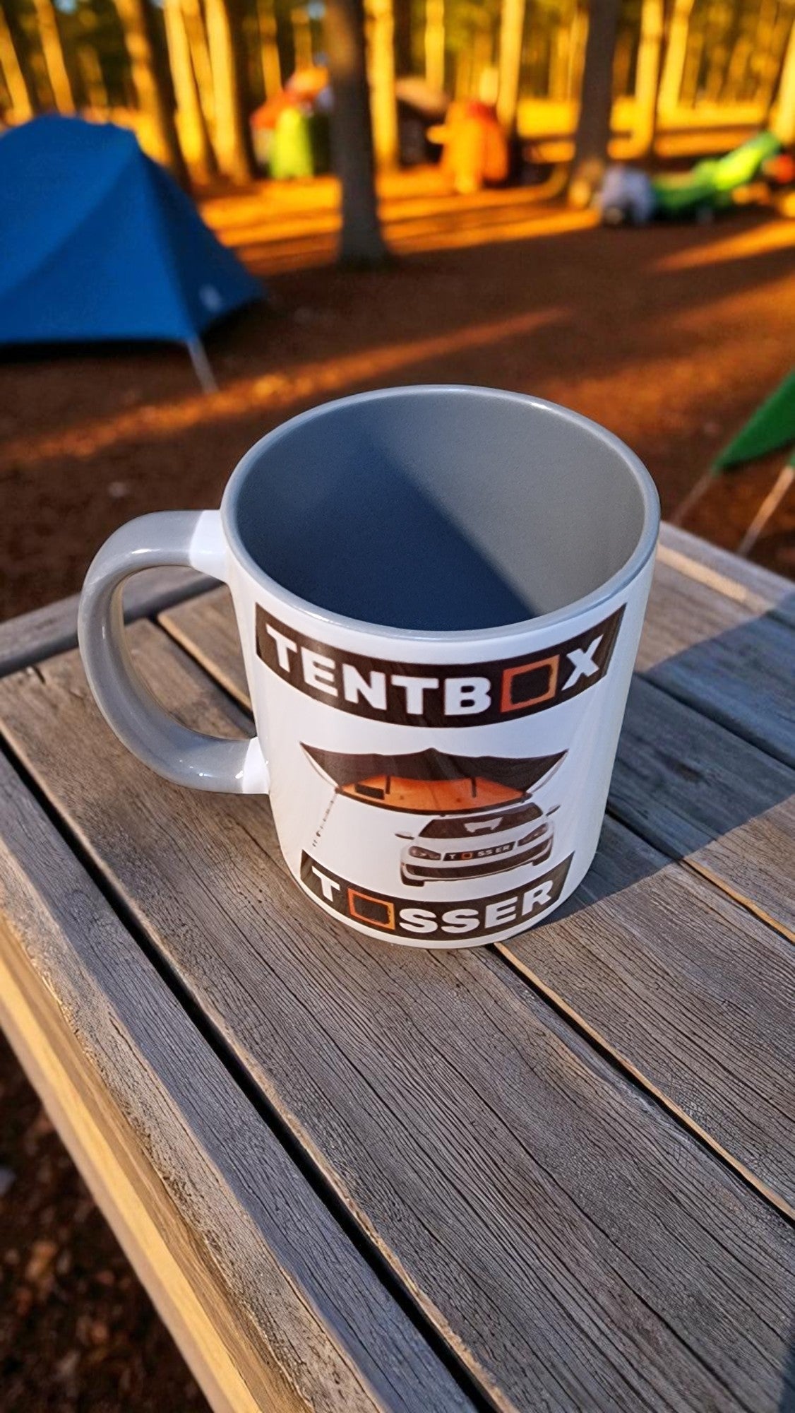 Mug with 'Tentbox' branding on a wooden surface outdoors.